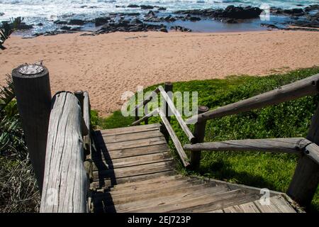 Holztreppe führt zum Strand mit sean und Felsen dahinter Stockfoto