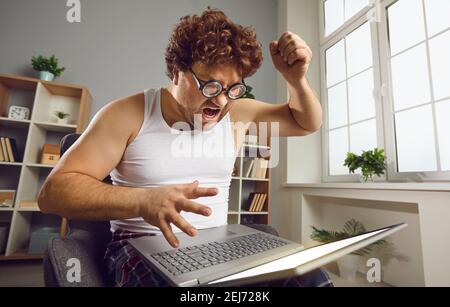 Lustiger nerdy Mann, der Problem mit seinem Laptop, schreien und drohen, es zu brechen Stockfoto