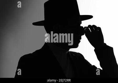 Silhouette eines Mannes in Jacke und stilvoller Hut Befestigung der Sonnenbrille Stockfoto