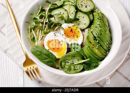 Quinoa-Schüssel mit Ei, Sonnenblumen-Mikrogemüse, Gurke, Avocado, Babyspinat in einer weißen Schüssel auf einem weißen Holztisch, türkische Küche Stockfoto