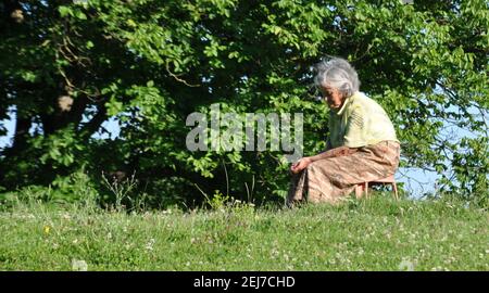 Alte verärgert Frau sitzt auf einem Stuhl am Rande des Waldes, Seitenansicht Stockfoto