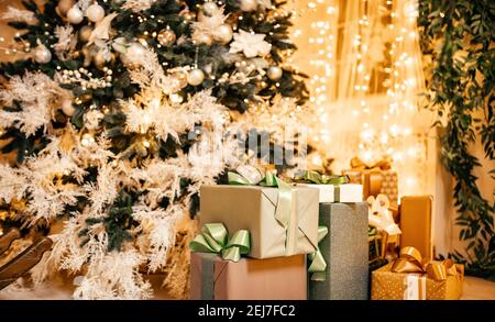 Geschenkboxen liegen unter Weihnachtsbaum im Innenraum, Bokeh im Hintergrund beleuchtet. Stockfoto