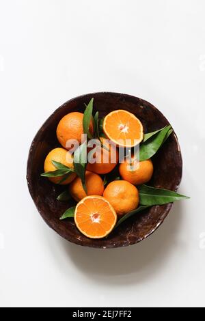 Frische Orangen, Mandarinen. Ganze und geschnittene Früchte mit grünen Blättern in braun handgemachte Keramik Schüssel White Tisch Hintergründe. Gesunde Rohkost Rahmen, Web Stockfoto