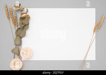 Weißes Einladungskarte Mockup mit getrocknetem Eukalyptus und goldenen Ohren Dekoration auf einem neutralen Tisch. 5x7-Verhältnis, ähnlich wie A6, A5 Kopierspeicher. Skandinavien Stockfoto