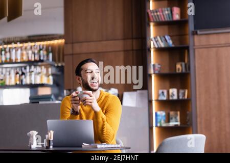 Aufgeregt arabischen Freiberufler lachen, während die Tasse Kaffee in halten Restaurant Stockfoto