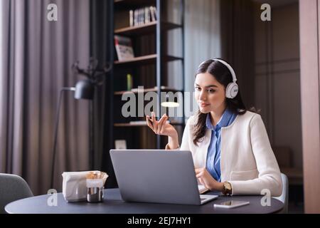 Junger Freiberufler in Kopfhörern sitzt in der Nähe Laptop im Restaurant Stockfoto