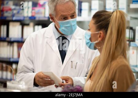 Maskierte Frau im Gespräch mit dem Apotheker in einer Apotheke, covid Coronavirus Konzept Stockfoto