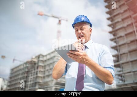 Architekt, der sein Mobiltelefon vor einer Baustelle benutzt Standort Stockfoto