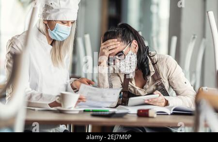Gastronomieunternehmer in einer verelenden Situation über Rechnungen sitzen in einem geschlossenen Restaurant. Stockfoto