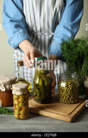 Frau schließt ein Glas eingelegter Gurken auf hölzernen Hintergrund Mit eingelegtem Essen Stockfoto