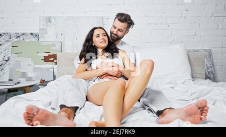Junger Mann umarmt fröhlich brünette freundin im Schlafzimmer Stockfoto