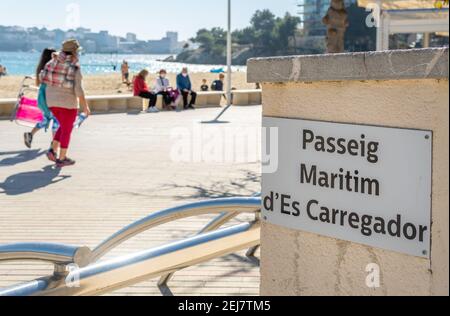 El Carregador maritime Promenade Zeichen in katalanischer Sprache, der mallorquinischen touristischen Ortschaft Palmanova. Im Hintergrund aus dem Fokus, Fußgänger Stockfoto