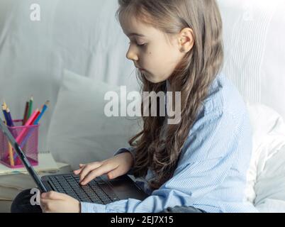 Ein Mädchen aus der Grundschule studiert zu Hause mit einem Laptop während der Quarantäne aufgrund der Coronavirus-Pandemie. Stockfoto