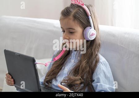 Ein Grundschülerin sitzt zu Hause auf der Couch mit einem Laptop in einer Online-Lektion während der Quarantäne wegen der Coronavirus-Pandemie. Stockfoto