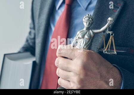 Rechtsanwalt hält Buch und Statue der Lady Justice, Nahaufnahme der Hand mit selektivem Fokus Stockfoto