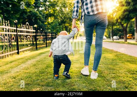 Mama hält die Hand ihres kleinen Kindes, geht im Park auf dem grünen Gras Stockfoto