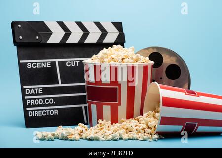 Klappbrett, Filmrolle und Eimer mit Popcorn auf blau, Kinokonzept Stockfoto