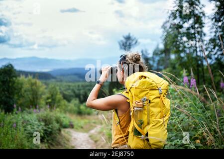 Rückansicht einer Wanderfrau mit Rucksack auf einer Wanderung in der Natur, mit Fernglas. Stockfoto