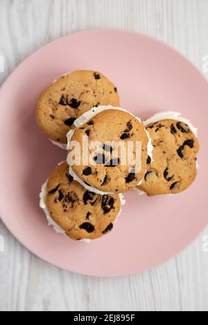 Hausgemachte Schokolade Chip Cookie Ice Cream Sandwich auf einem rosa Teller auf einem weißen Holzhintergrund, Draufsicht. Über Kopf, von oben, flach liegend. Stockfoto