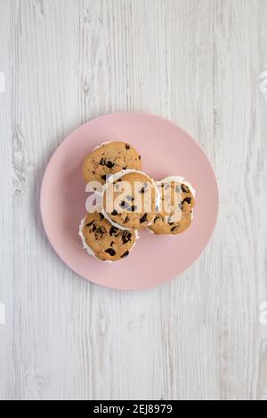Hausgemachte Schokolade Chip Cookie Ice Cream Sandwich auf einem rosa Teller auf einem weißen Holztisch, Draufsicht. Über Kopf, von oben, flach liegend. Stockfoto