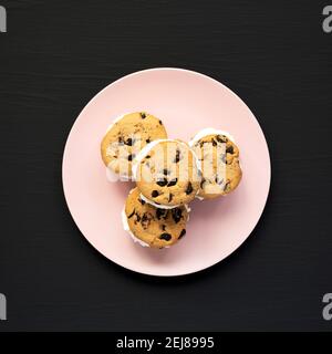 Hausgemachte Schokolade Chip Cookie Ice Cream Sandwich auf einem rosa Teller auf einem schwarzen Hintergrund, Draufsicht. Über Kopf, von oben, flach liegend. Stockfoto