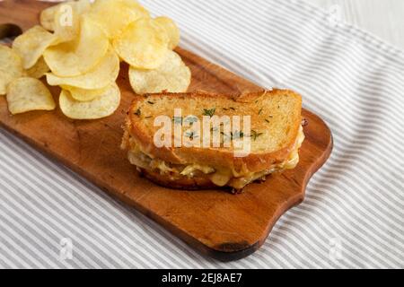 Hausgemachtes French Onion Melt Cheese Sandwich mit Chips auf einem rustikalen Holzbrett, Seitenansicht. Stockfoto