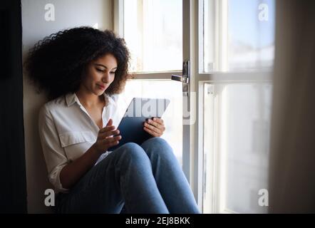 Portrait der jungen Frau auf Fensterbank drinnen zu Hause, mit Tablet. Stockfoto