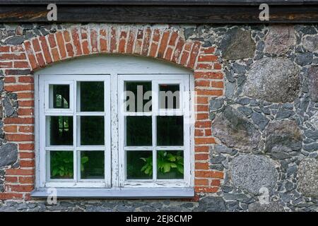 Fenster mit einem Rahmen mit alten verwitterten Farbe bedeckt, auf einer Steinmauer, in roten Ziegelsteinen gerahmt. Aus den Fenstern der Welt-Serie. Stockfoto