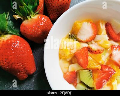 Schüssel mit frischem Obstsalat umgeben von einer Auswahl frisch zubereiteter Früchte. Stockfoto