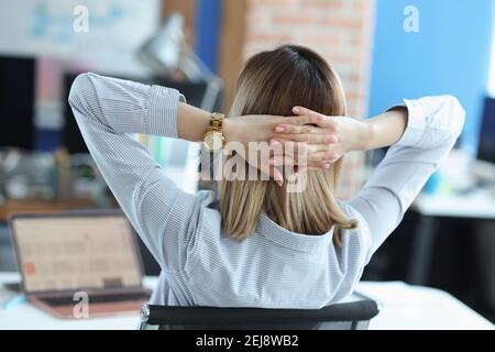 Frau, die am Tisch sitzt und ihre Hände hinter dem Kopf hält Stockfoto