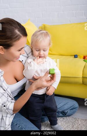Lächelnde Frau gibt Spielzeug Würfel Baby Junge während des Spielens Auf dem Boden zu Hause Stockfoto