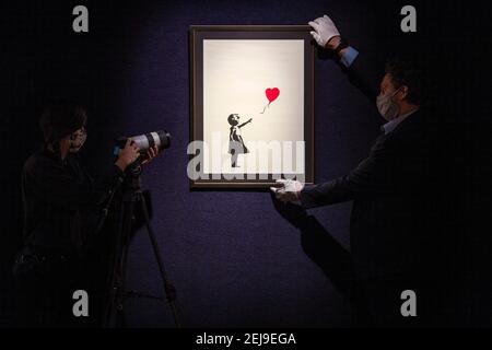 Ein Galerist wird gefilmt und schaut auf 'Girl with a Balloon' von Banksy, zu sehen in Bonhams London vor den kommenden Briten. Cool. Verkauf mit Kunstwerken, Fotografien, Designer-Mode und Unterhaltung Erinnerungsstücke. Bilddatum: Montag, 22. Februar 2021. Stockfoto