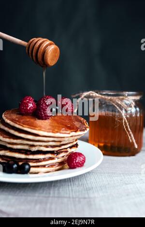 Saftige Pfannkuchen mit Beeren und Honig auf einem weißen Teller, Löffel, Glas, Holztisch. Hochwertige Fotos Stockfoto