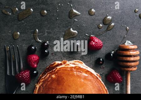 Saftige Pfannkuchen mit Beeren, Honig, Löffel auf einem schwarzen und grauen Betontisch. Hochwertige Fotos Stockfoto