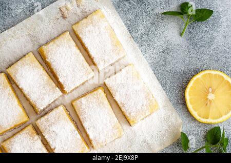 Zitronenquadrate auf Backpapier, eine Scheibe Zitronen- und Minzblätter, auf grauem Hintergrund. Stockfoto