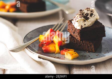 Brownies mit Sahne und Schokolade auf der Oberseite, Pfirsichstücke in hellblauen Tellern mit Gabeln und einer weißen Serviette, auf weißem Hintergrund. Stockfoto