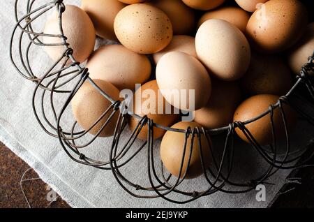 Eier in einem Wired-Korb auf einer beigen Serviette und dunklem Hintergrund. Stockfoto