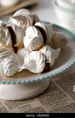 Meringue Cookies mit Dulce de leche auf einem weißen und grünen Kuchenständer und auf einer alten Zeitschrift, mit einigen Teetassen im Hintergrund. Stockfoto