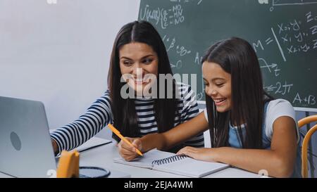 Mutter lächelt und Blick auf Laptop in der Nähe glücklich Tochter tun Hausaufgaben Stockfoto