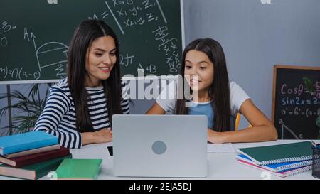 Glückliche Mutter und Tochter, die sich einen Laptop in der Nähe von Notebooks angeschaut haben Tabelle Stockfoto