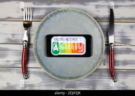 Viersen, Deutschland - Februar 9. 2021: Nahaufnahme des Smartphone-Bildschirms mit Logo-Schriftzug von Nutri-Score auf Teller mit Besteck Stockfoto