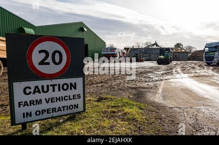 East Lothian, Schottland, Großbritannien, 22nd. Februar 2021. Karottenernte: Luffness Mains Farm Eingangsschild und 20 mph Geschwindigkeitsbegrenzung Warnung mit Karotten Ernte Landmaschinen im Hof Stockfoto
