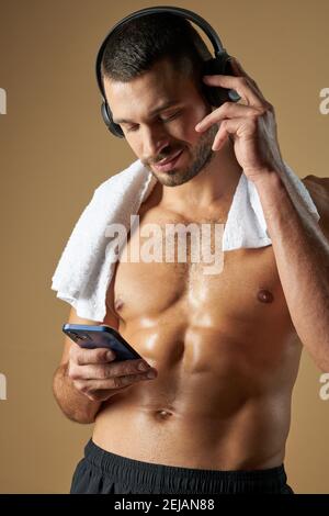 Waist up Porträt von glücklich lächelnden Erwachsenen Sportler mit Handtuch Auf der Schulter stehend im Zimmer, während er das Handy benutzte Stockfoto