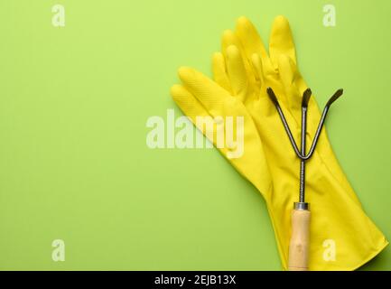 Gelbe Gummihandschuhe und Metall Garten kleine Rechen auf grünem Hintergrund, kopieren Raum Stockfoto