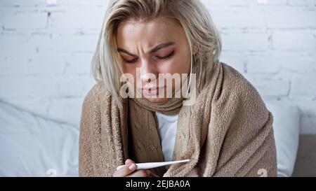 Junge kranke Frau, die Thermometer im Schlafzimmer ansieht Stockfoto