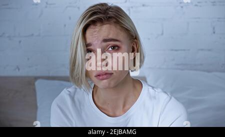 Unzufriedene kranke Frau, die im Schlafzimmer auf die Kamera schaut Stockfoto
