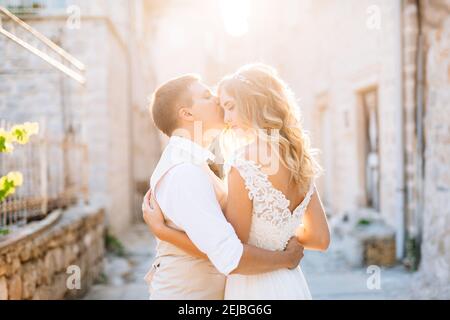 Die Braut und der Bräutigam stehen umarmt auf den Straßen von Perast, der Bräutigam küsst die Braut auf die Stirn Stockfoto