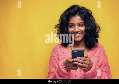 Schöne Sri Lanka Mädchen macht Technologie Posen mit gelb hell Hintergrund - Junge Frau nutzt Handy zu chatten und Messaging Stockfoto