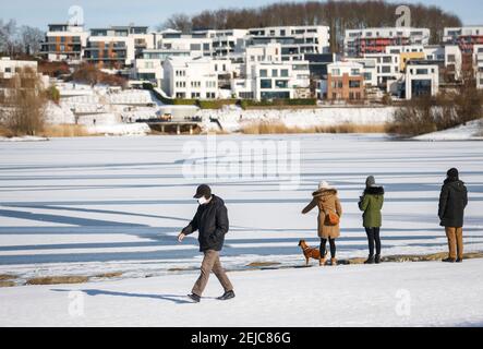 Dortmund, Ruhrgebiet, Nordrhein-Westfalen, Deutschland - Spaziergänger am Phoenix See im Winter in Eis und Schnee in Zeiten der Corona Pandemie mit Maske, hinten Stockfoto