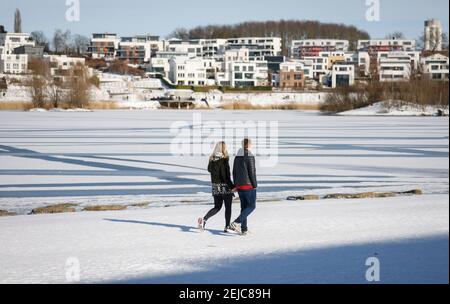 Dortmund, Ruhrgebiet, Nordrhein-Westfalen, Deutschland - Spaziergänger am Phoenix See im Winter mit Eis und Schnee, Luxus-Eigentumswohnungen und Häuser im Hintergrund Stockfoto